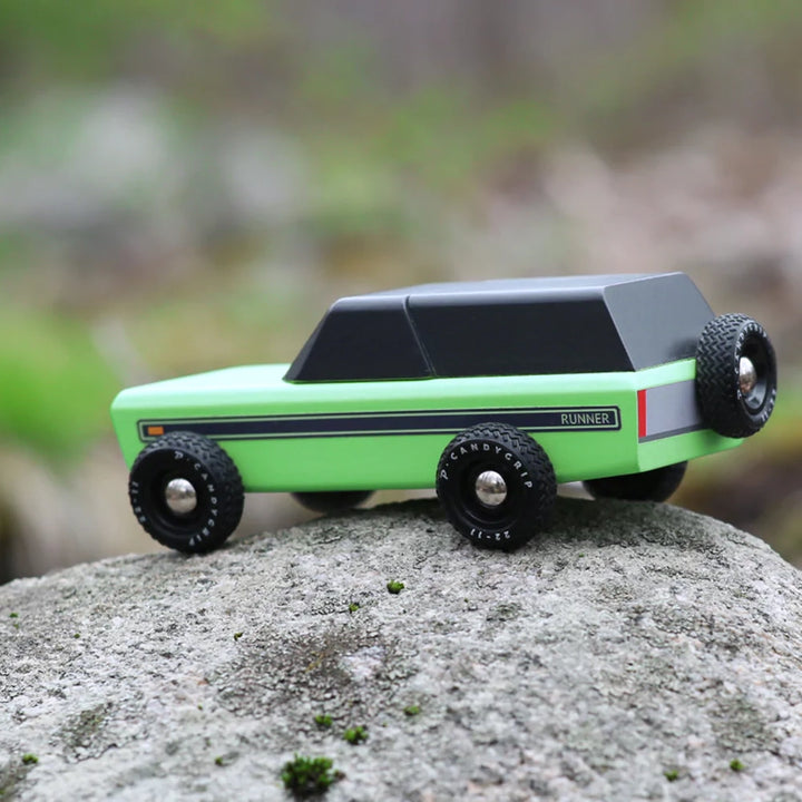 A Candylab Runner vintage children's wooden toy vehicle resting outside on a rock, showing off its outdoor appeal.