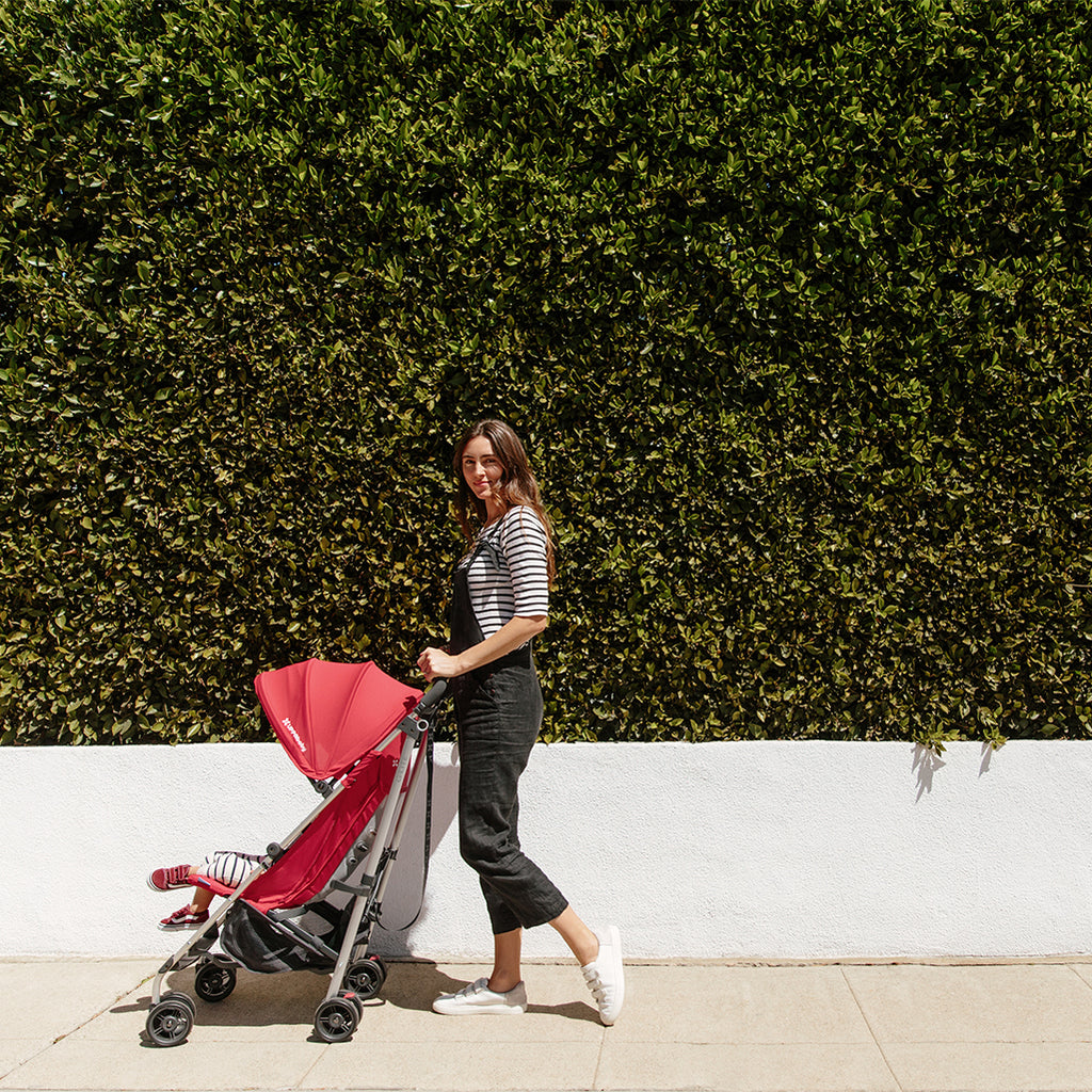 Mom pushing baby in UPPAbaby G-Lite Lightweight Stroller in red