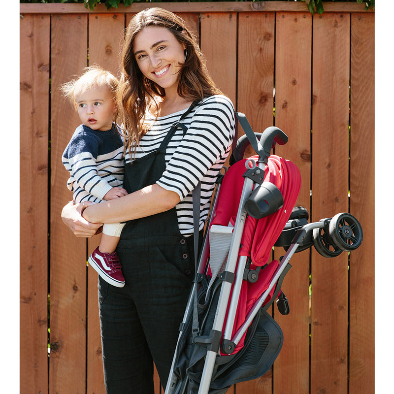 Mom Carrying Baby and Folded UPPAbaby G-Lite Lightweight Stroller in red