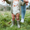 Lifestyle image of baby wearing boots and walking with help of parent.