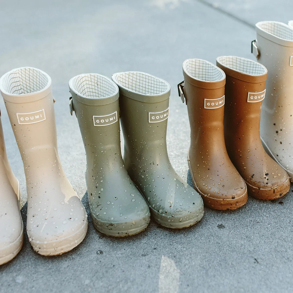 Lifestyle image of multiple pairs of goumikids Muddies boots lined up together and covered in water and outside debris.