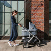 Woman Pushing Uppababy Cruz Stroller with Bassinet Accessory in Greyson