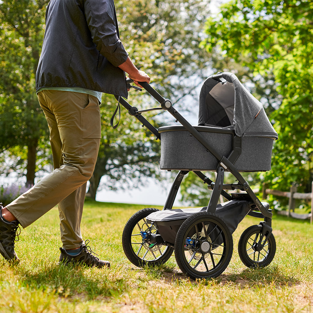 Man Pushing Uppababy Cruz Stroller with Bassinet Accessory on Grass