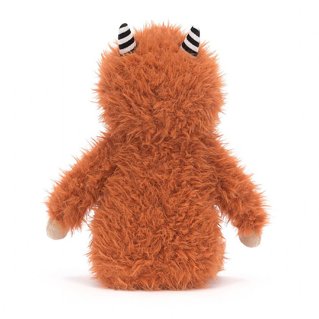 Jellycat Pip Monster Stuffed Animal Children's Toy. Burnt orange furry monster with tan face, hands, and feet. Two black and white striped horns on top of its head. Wide eyes and small brown nose with little stitched smile. Back view.