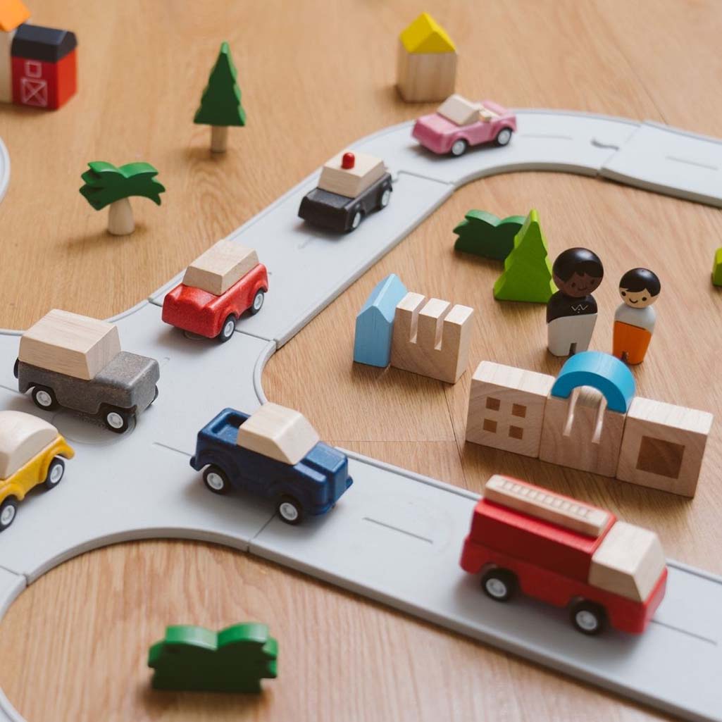 A Plan Toys wooden police car at play, surrounded by other wooden toy vehicles for pretend adventures.