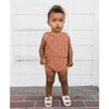 lifestyle_1, Terry cloth playsuit with elasticized waist and snaps for easy changes. Red clay back ground with red and white rainbow print. Child standing wearing romper.