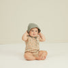 lifestyle_1, Sleeveless romper with elastic leg openings and snap button bottom closure for easy on and off. child sitting on the ground wearing a  bonnet and romper.