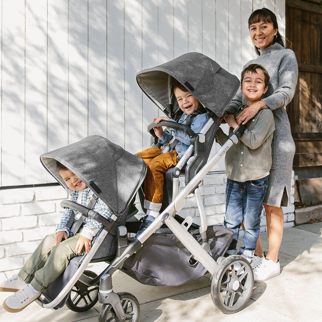Mom walking with three siblings using UPPAbaby VISTA V2 Double Stroller with Piggyback Sibling Board