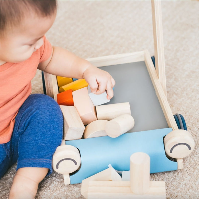 Plan Toys Baby Walker Infant Toddler Push Toy & Blocks Set - A child is grasping a light blue block and engaging in open ended play