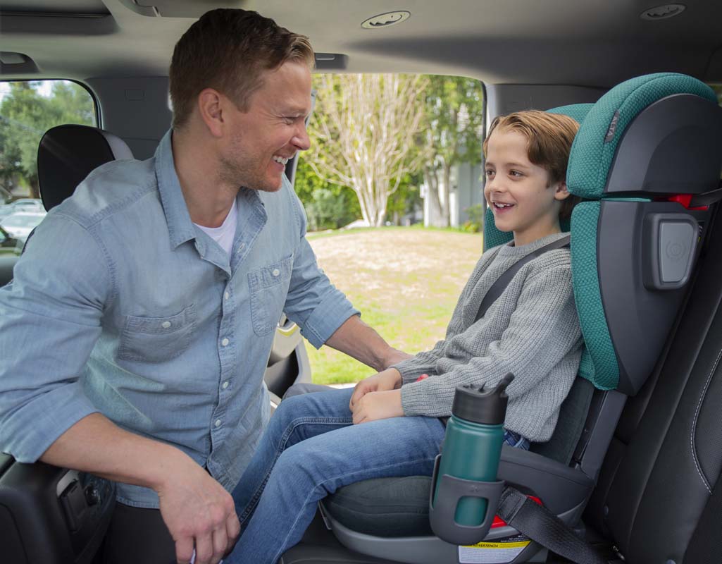 Parent smiling at child in Uppababy Teal Luca Alta booster seat in car