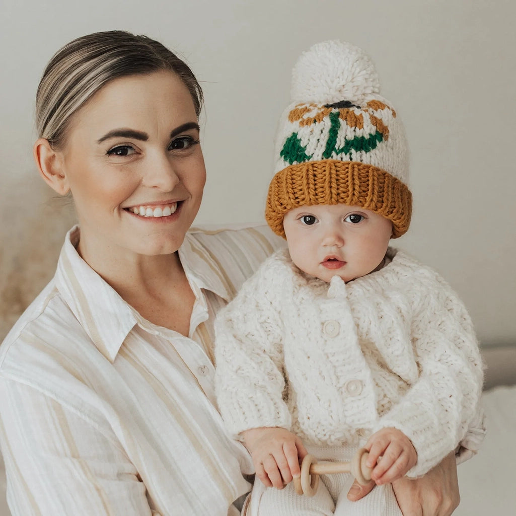 Huggalugs Coneflower Gold Hand Knit Beanie Infant & Toddler Hat modeled on infant with parent.