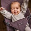 infant smiling with arms raised in purple bouncer seat by babybjorn