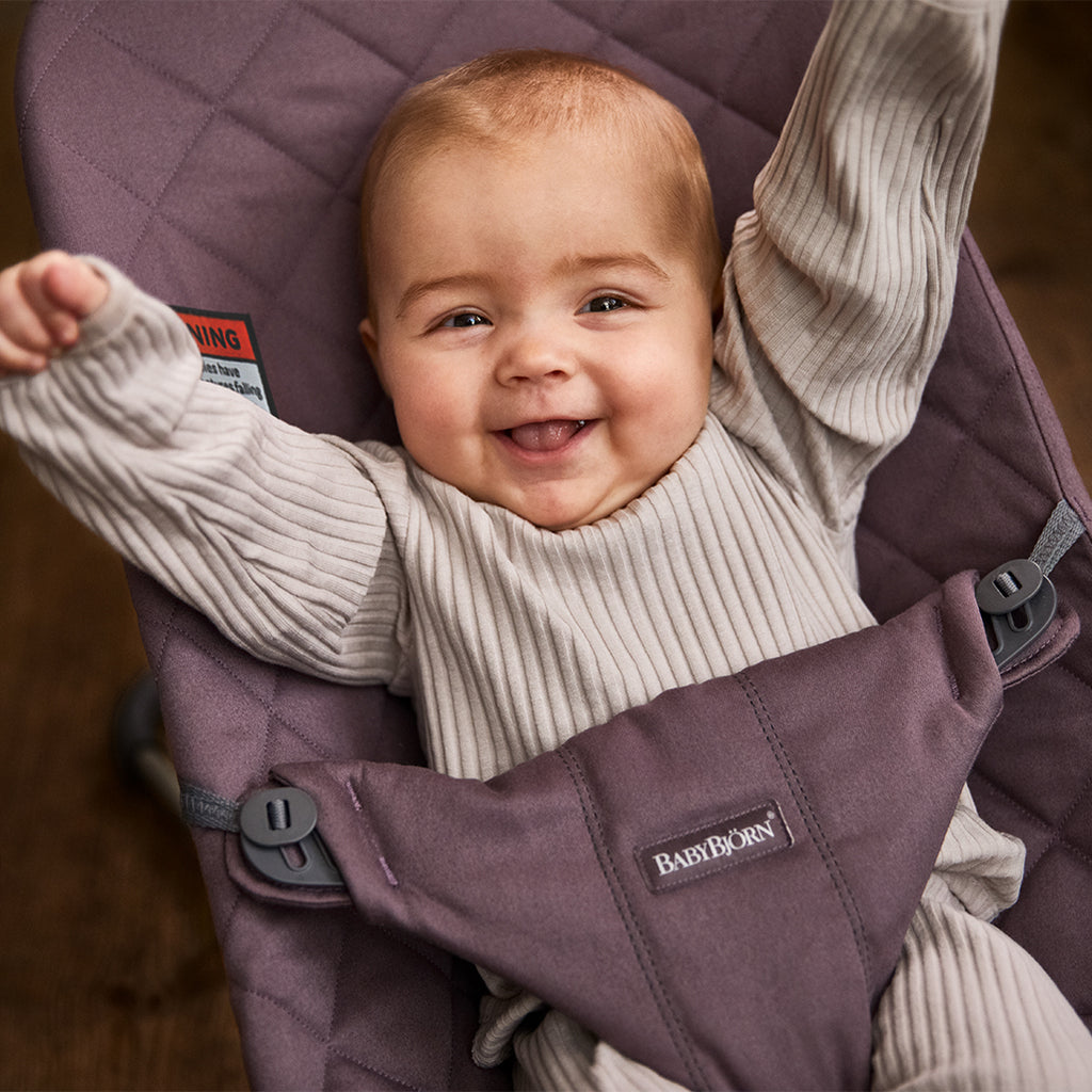 infant smiling with arms raised in purple bouncer seat by babybjorn