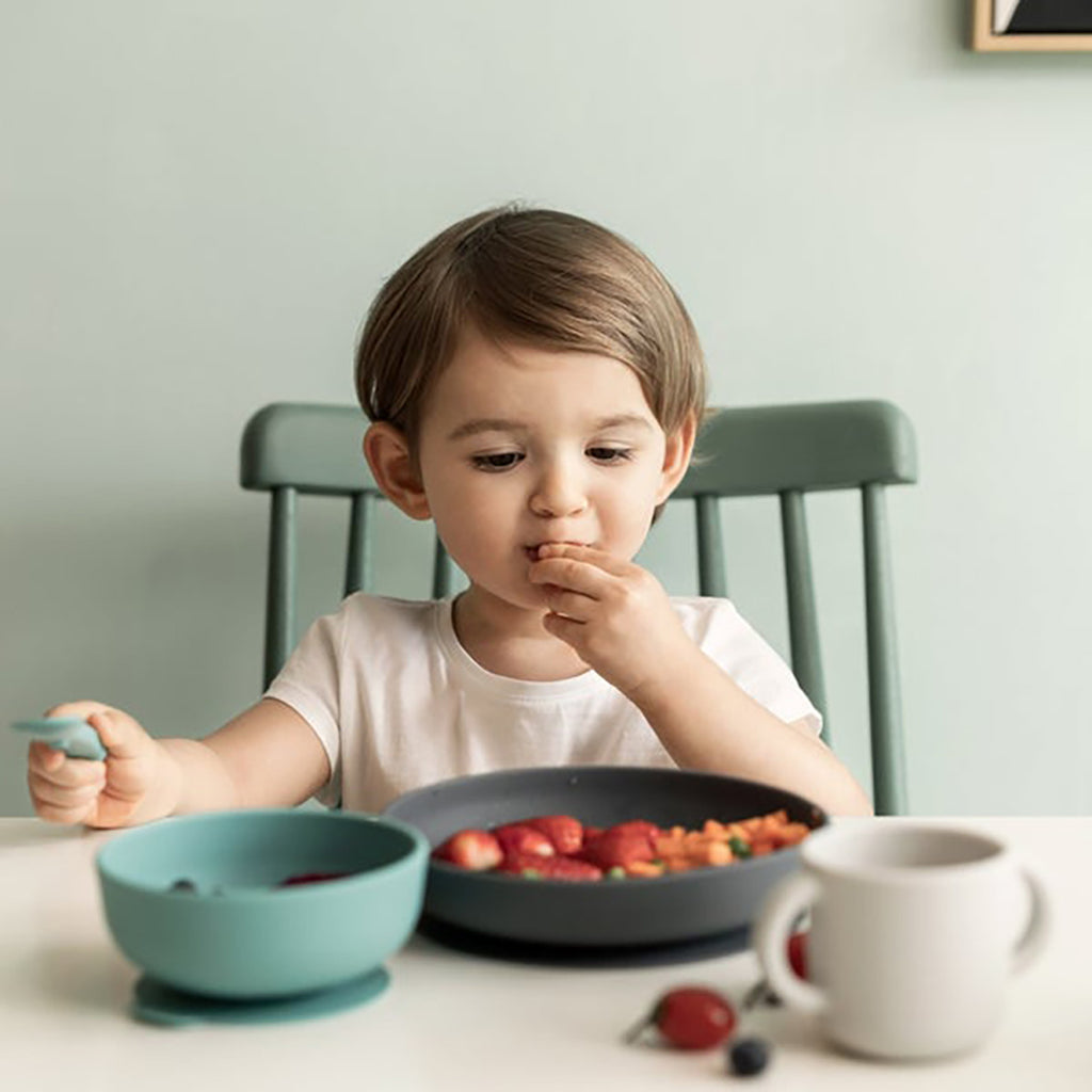 lifestyle_1 EKOBO Lagoon Suction Silicone Baby Meal Set - child eating strawberries and using all components of the set 