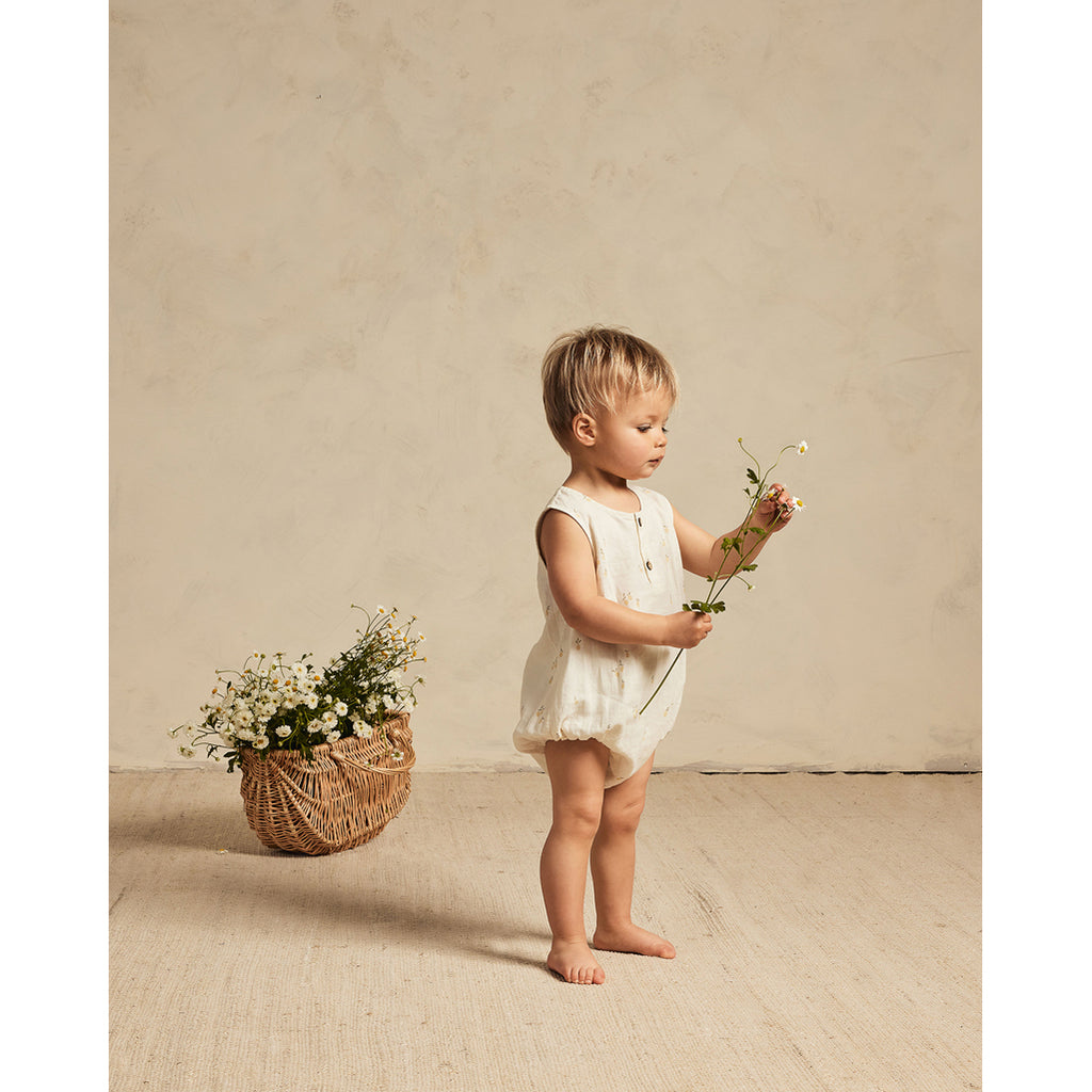 Baby wearing Rylee & Cru lemon romper holding a flower.