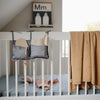 baby crib with mushie product hanging on rail with yellow blanket
