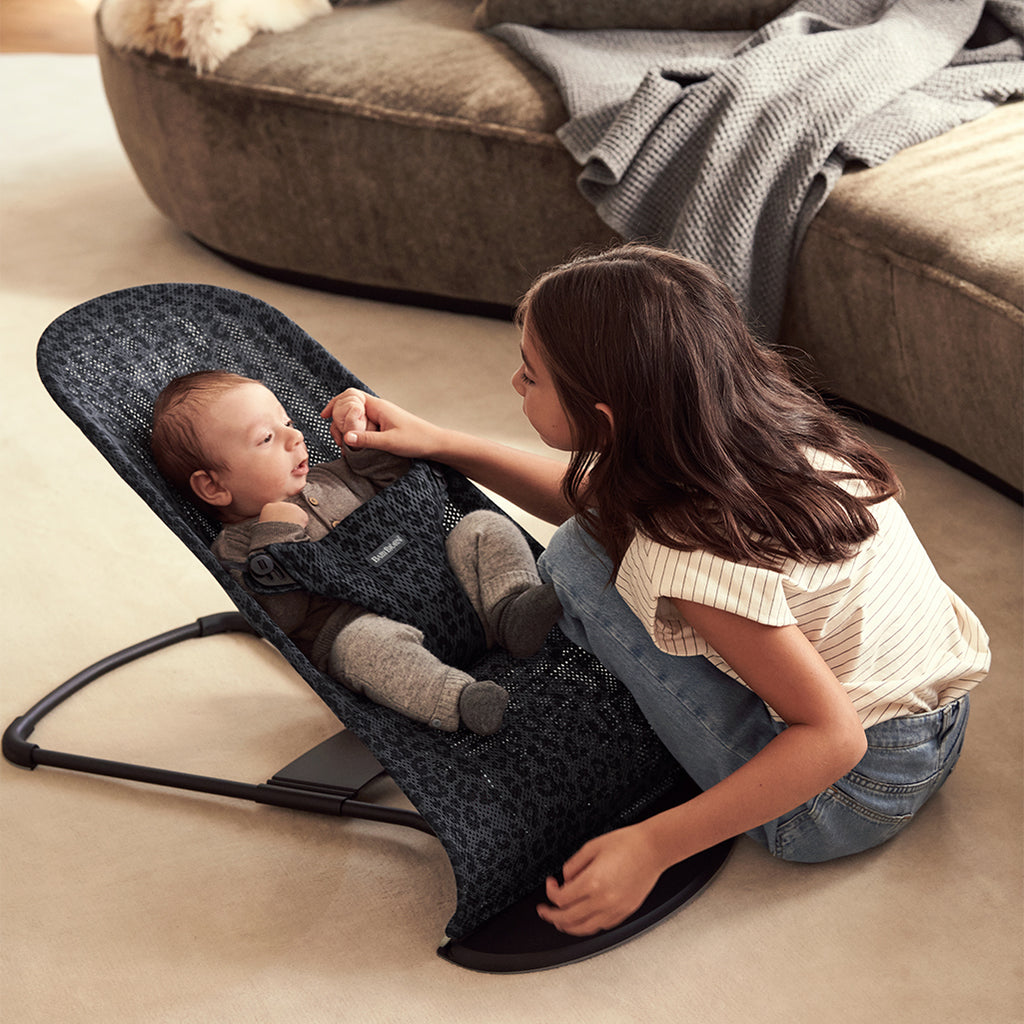 sister and infant playing in leopard print anthracite mesh bouncer seat by babybjorn