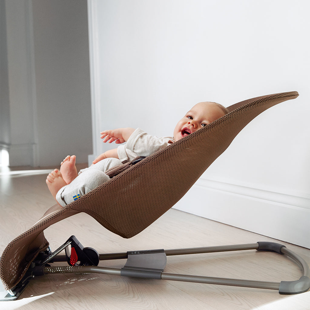 baby smiling and facing sideways in cocoa brown baby bouncer from baby bjorn