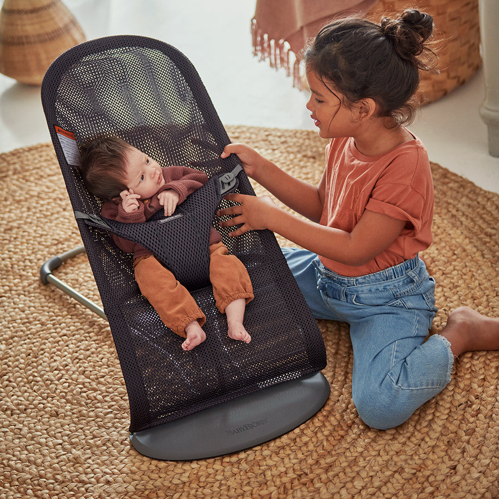 sister attending to baby in anthracite mesh babybjorn bouncer bliss