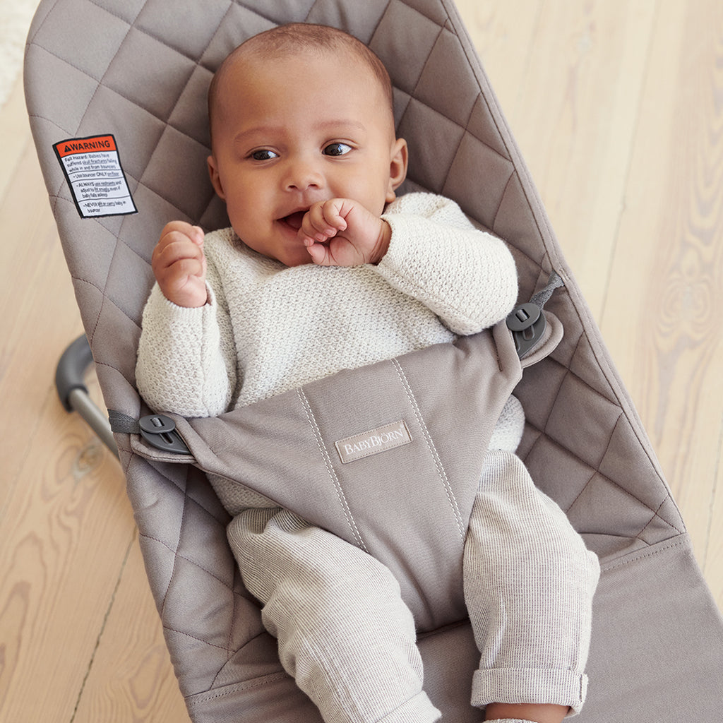 baby smiling in sand grey cotton quilt baby bouncer by Babybjorn
