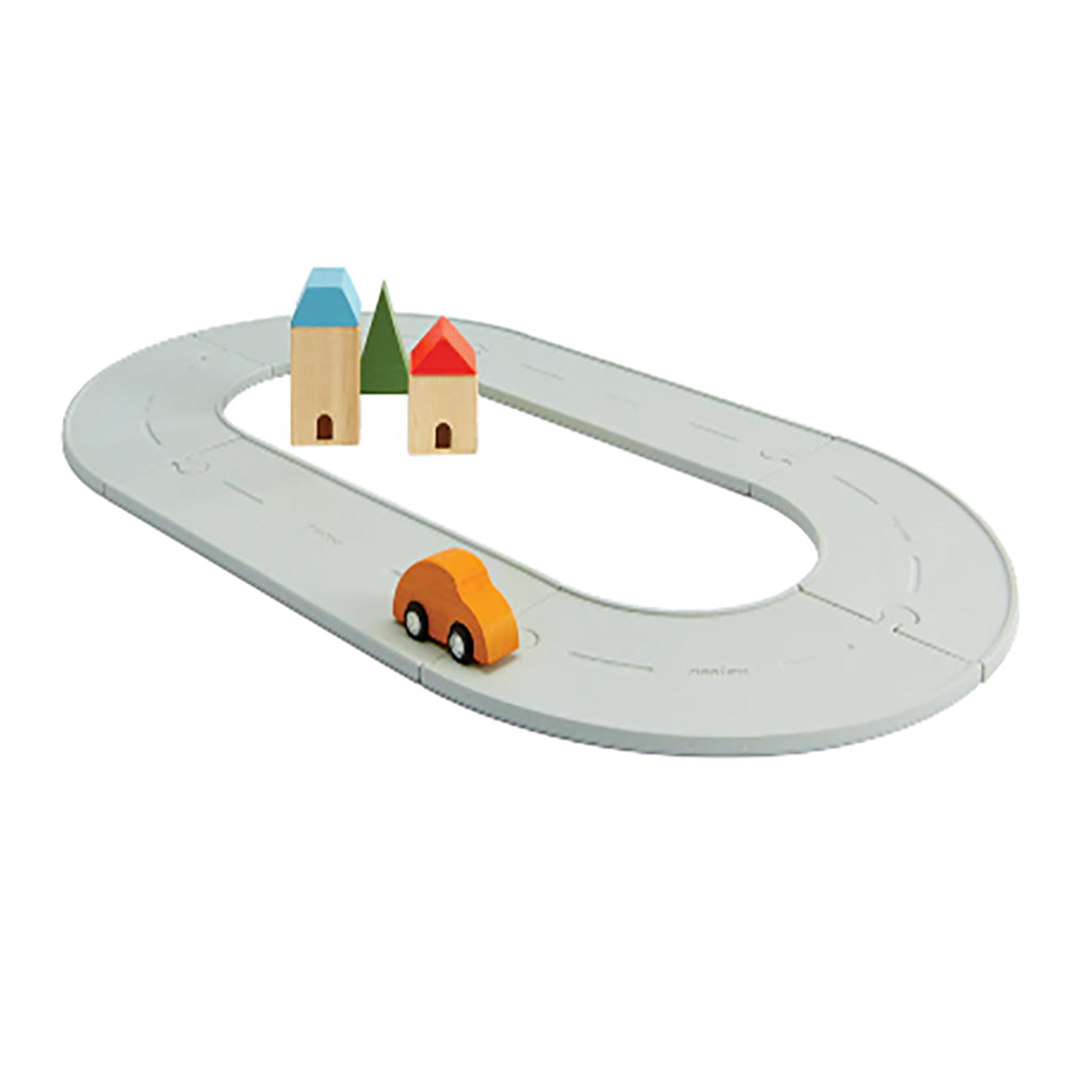 A small Plan Toys road & rails rubber toy track set featuring grey circular tracks and wooden toy houses and trees.