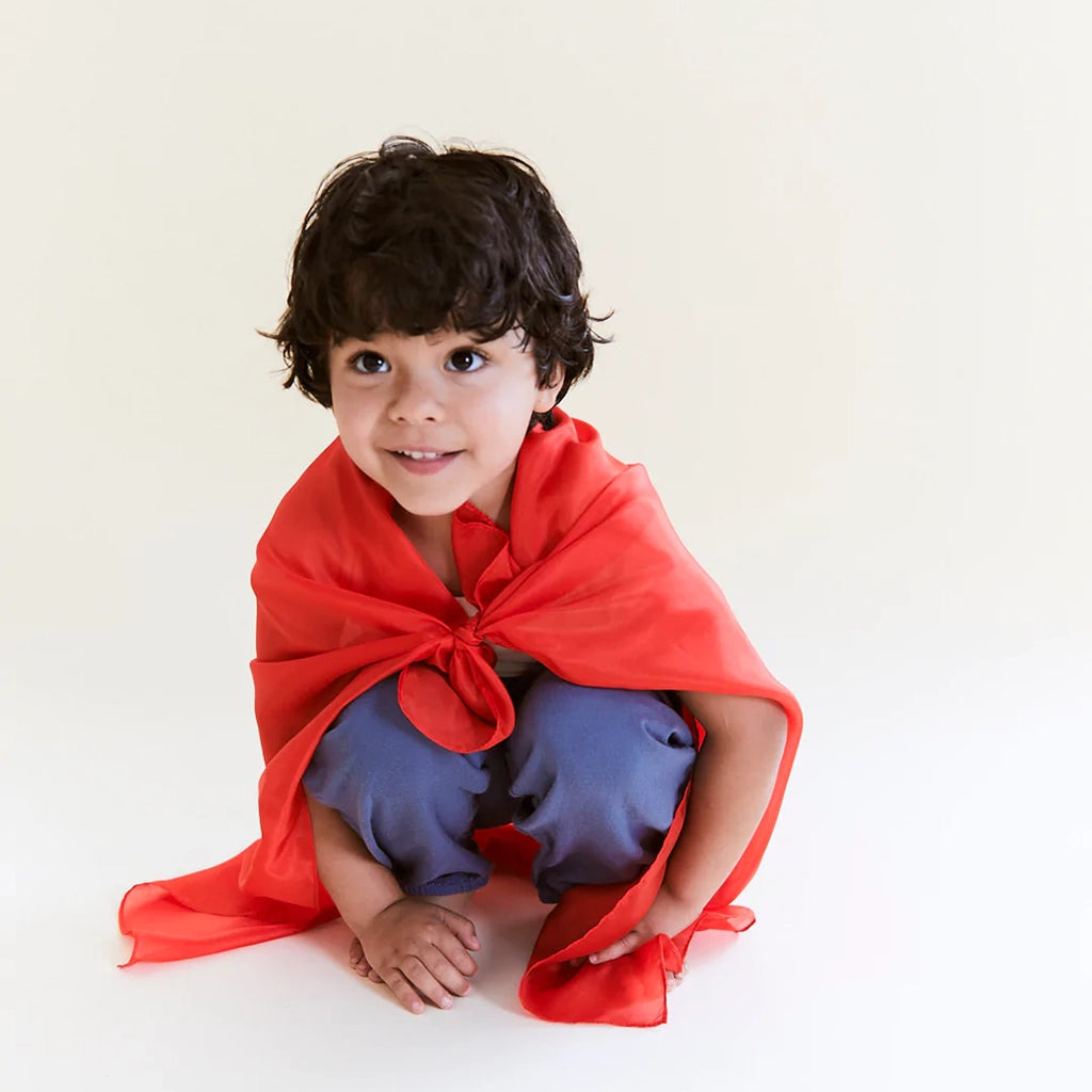 Lifestyle image of a child modeling a red Playsilk as a cape.