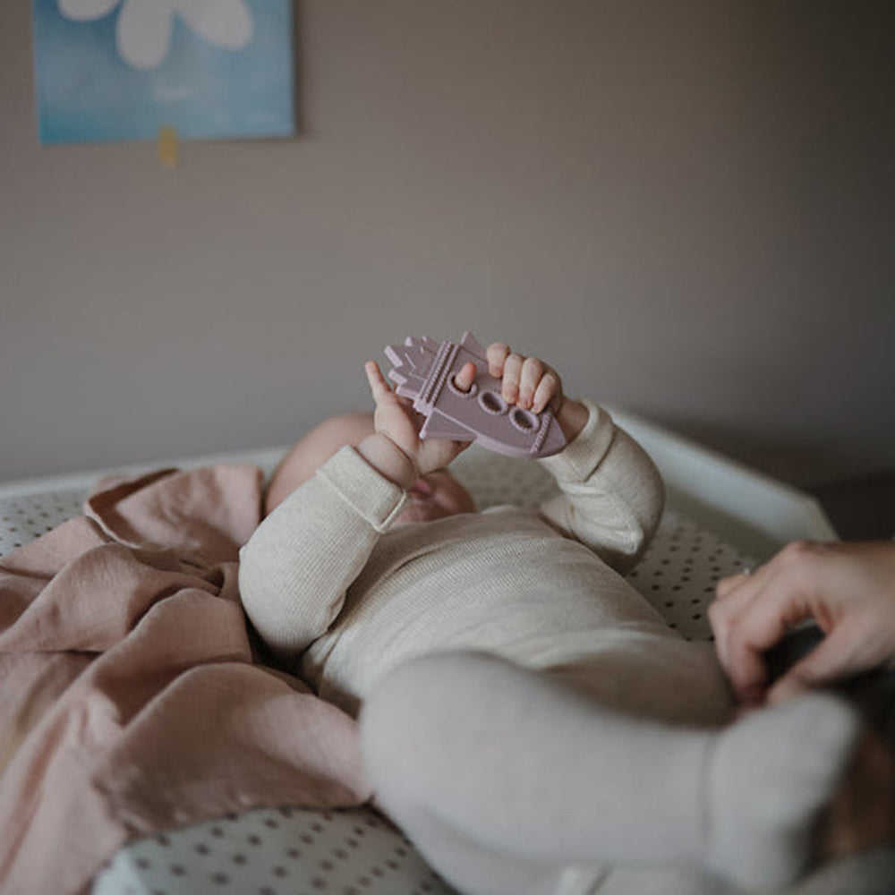 Infant holding a Mushie lilac rocket teether for soothing teething pain