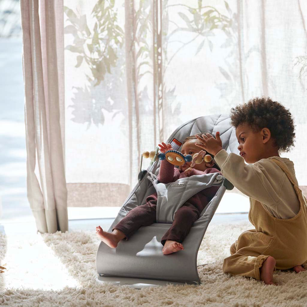 babies playing with Babybjorn bouncer toy in bouncer bliss light grey cotton petal quilt